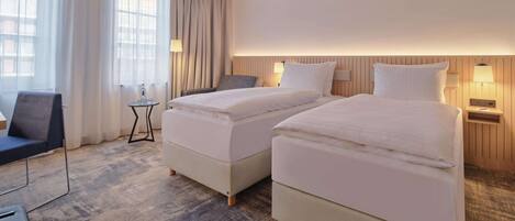 Une chambre d’hôtel avec deux lits, un bureau, une chaise et une vue sur l’extérieur grâce à de grandes fenêtres.