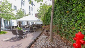 An outdoor patio with tables and chairs, a white tent, a red fire hydrant, and a building with a white facade. - Dorint Hotel Würzburg (Würzburg)