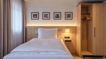 Habitación de hotel con una cama bien hecha, una mesita de noche con lámpara, un armario y cuatro cuadros enmarcados en la pared.