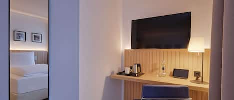 A hotel room with a bed, a desk with a chair, a TV, a lamp, and a mirror.