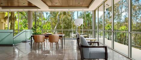 A spacious indoor area with large windows, a staircase, and seating arrangements.