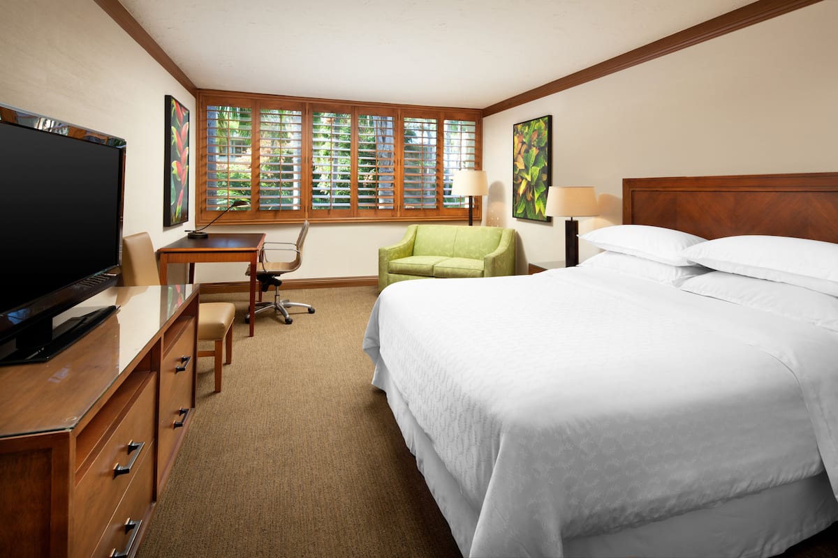A hotel room with a bed, a desk, a television, and a window with blinds.