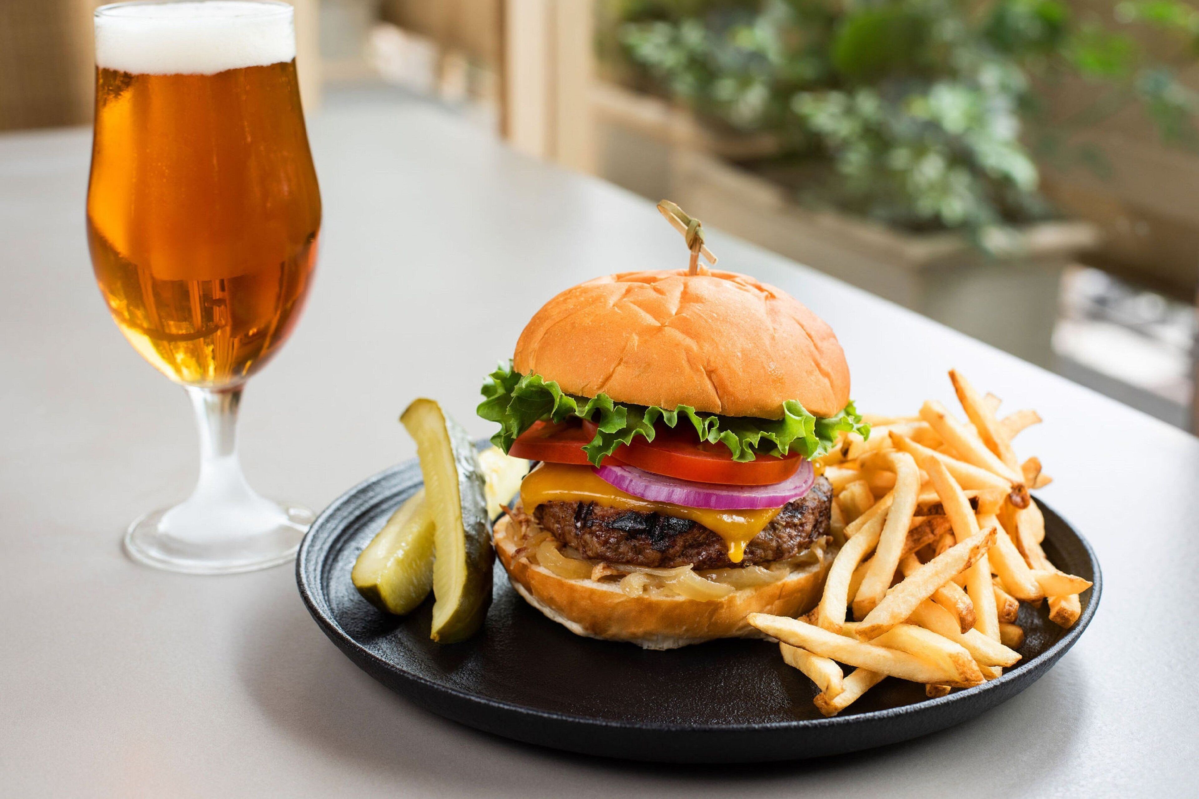A burger with fries and a glass of beer on a plate.