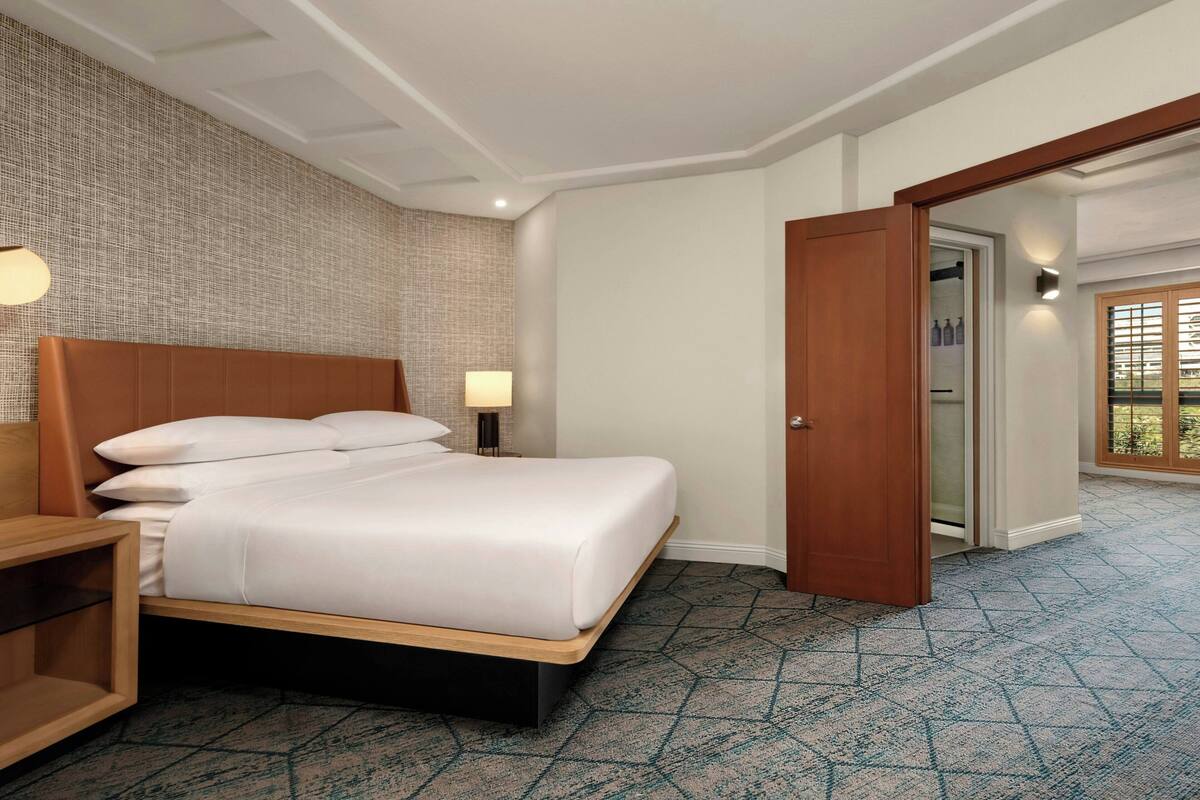 A hotel room with a bed, a nightstand, a lamp, a wooden door, and a patterned carpet.