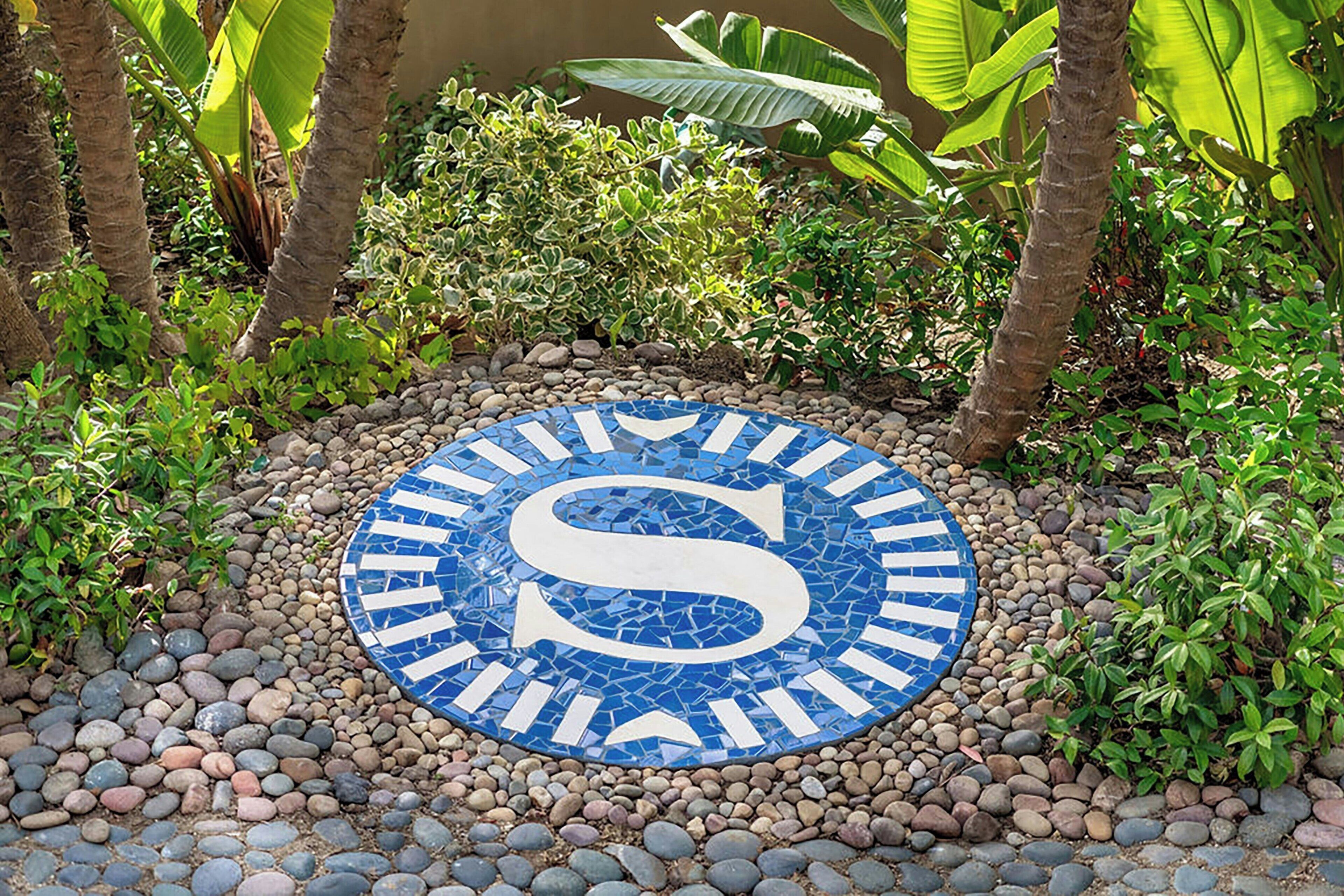 A mosaic with a large letter 'S' surrounded by a circular pattern of stones and greenery.