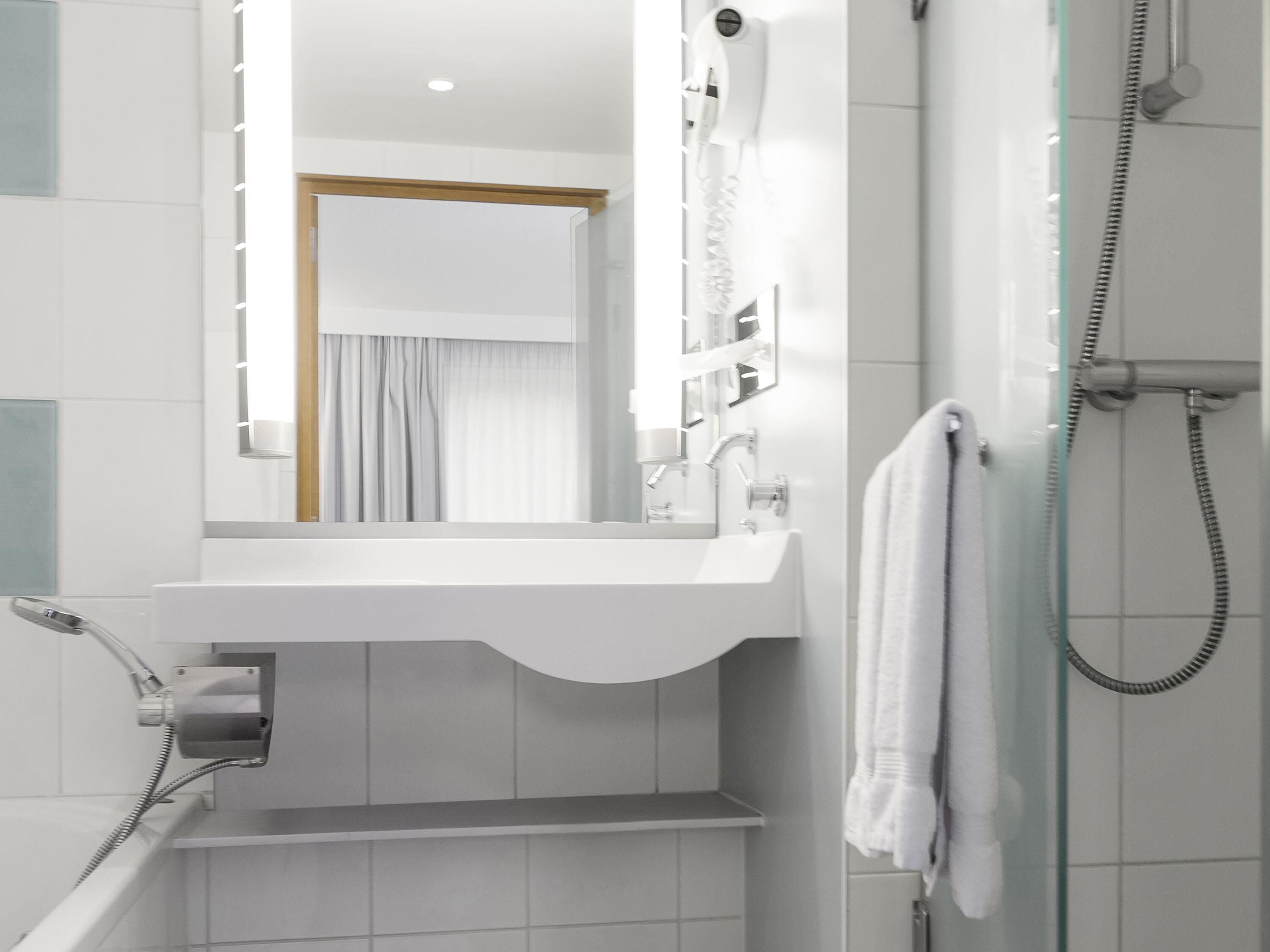 Un baño con lavamanos blanco, espejo y ducha.