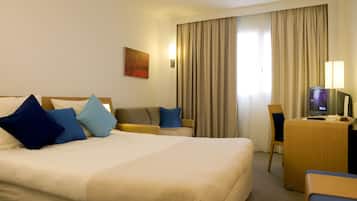 Een hotelkamer met een groot bed, een bureau met een computer, een stoel en een televisie.
