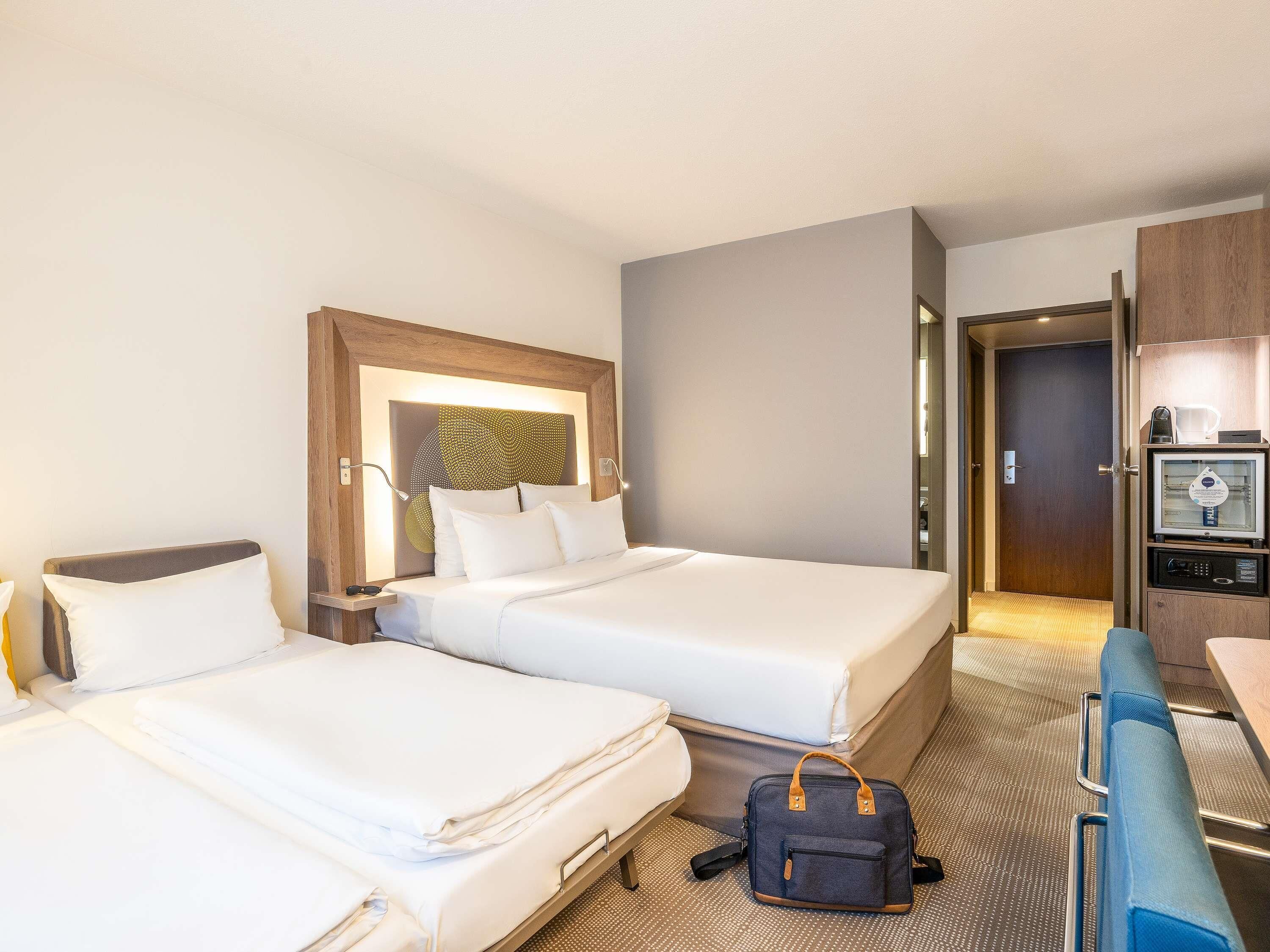 A hotel room with two beds, a desk, a chair, a coffee machine, and a minibar.