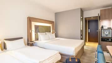 A hotel room with two beds, a desk, a chair, a coffee machine, and a minibar.