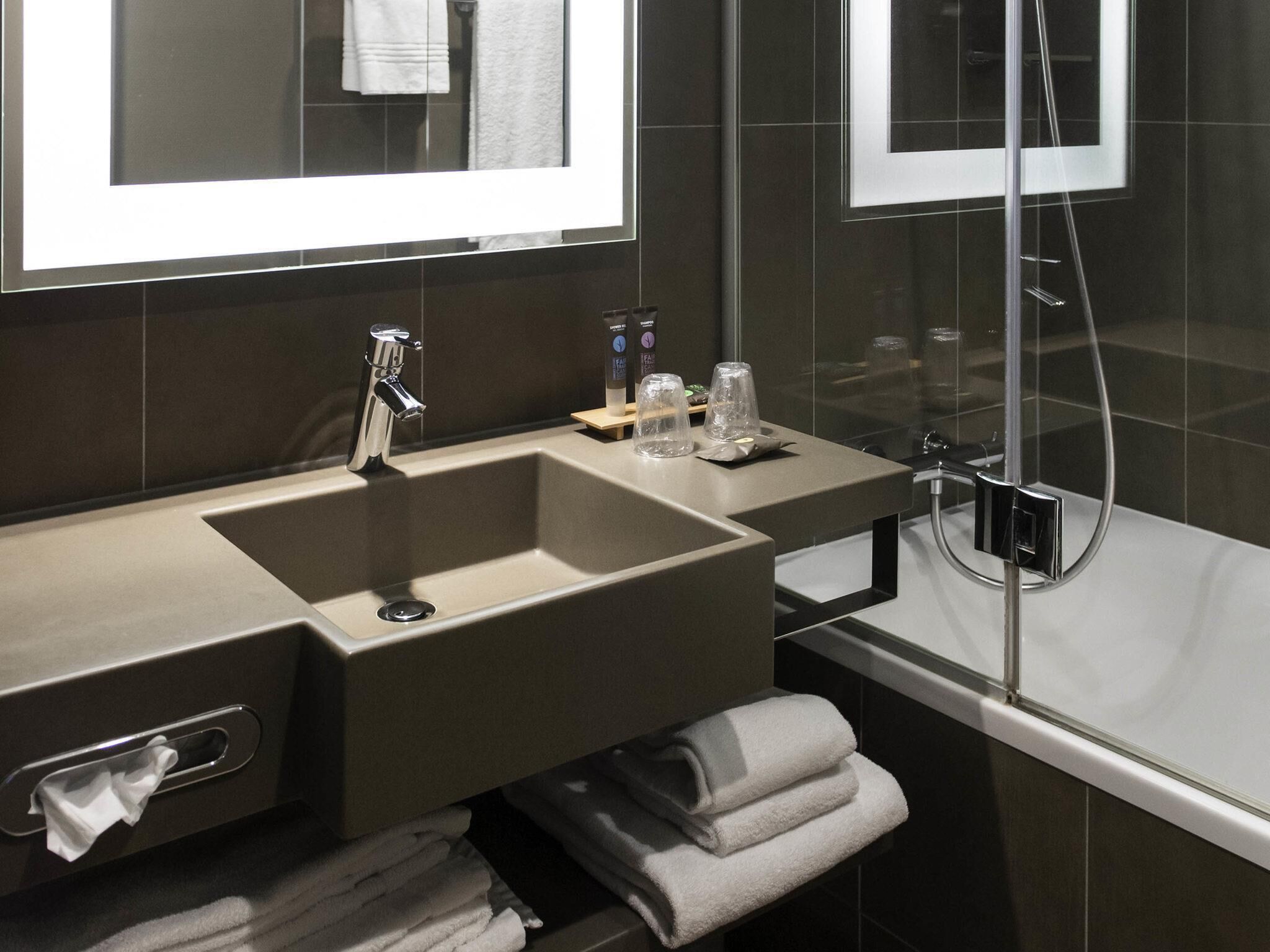 Une salle de bain moderne avec un grand lavabo, un miroir, un porte-serviettes et une douche à parois de verre.