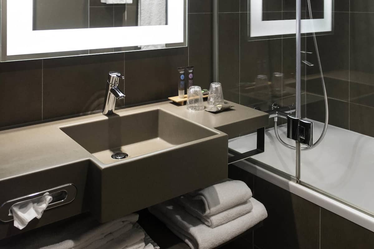 A modern bathroom with a large sink, a mirror, a towel rack, and a glass shower enclosure.