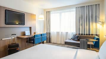 A hotel room with a bed, a desk, a chair, a sofa, a TV, and a window with curtains.