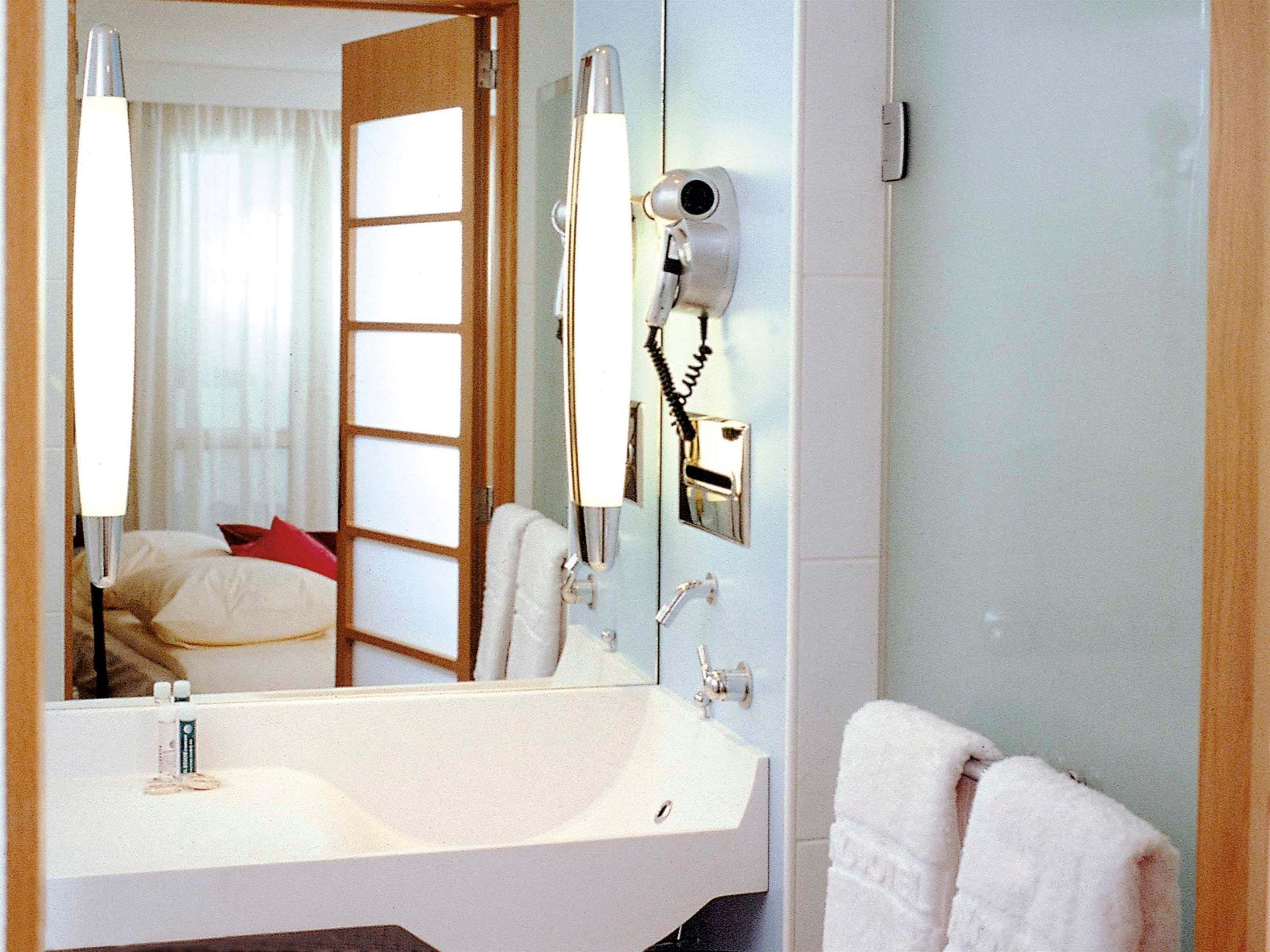Un baño de hotel con un espejo grande, un lavamanos, un secador de pelo y un perchero para toallas.