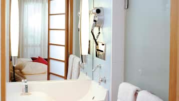 Un baño de hotel con un espejo grande, un lavamanos, un secador de pelo y un perchero para toallas.