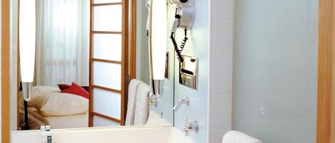 A hotel bathroom with a large mirror, a sink, a hairdryer, and a towel rack.