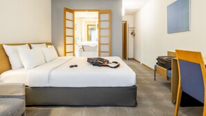 Habitación de hotel con cama, escritorio, silla, maleta y un cuadro en la pared.