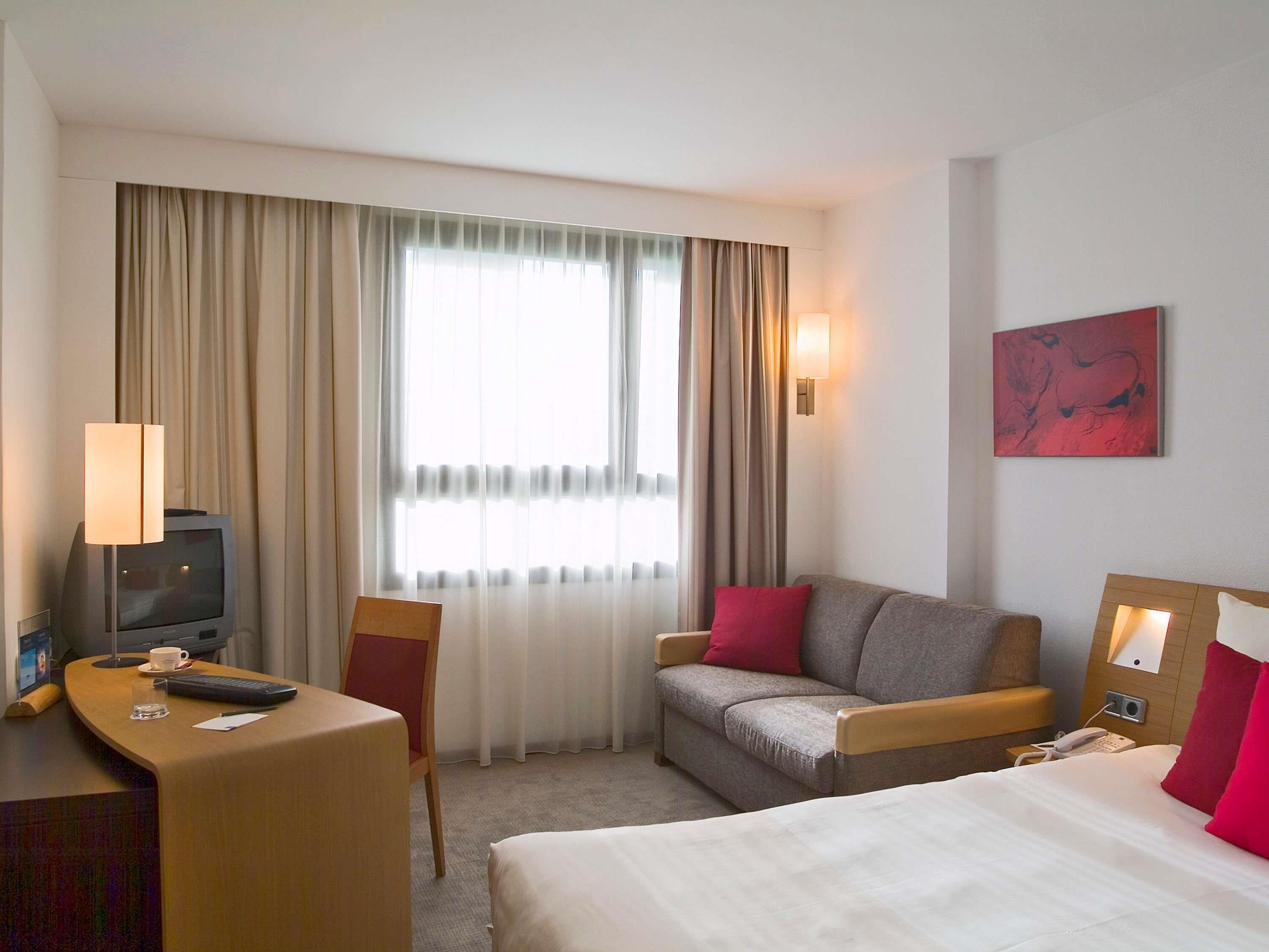 Ein Hotelzimmer mit Bett, Schreibtisch mit Computer, Stuhl, Sofa und Fernseher.