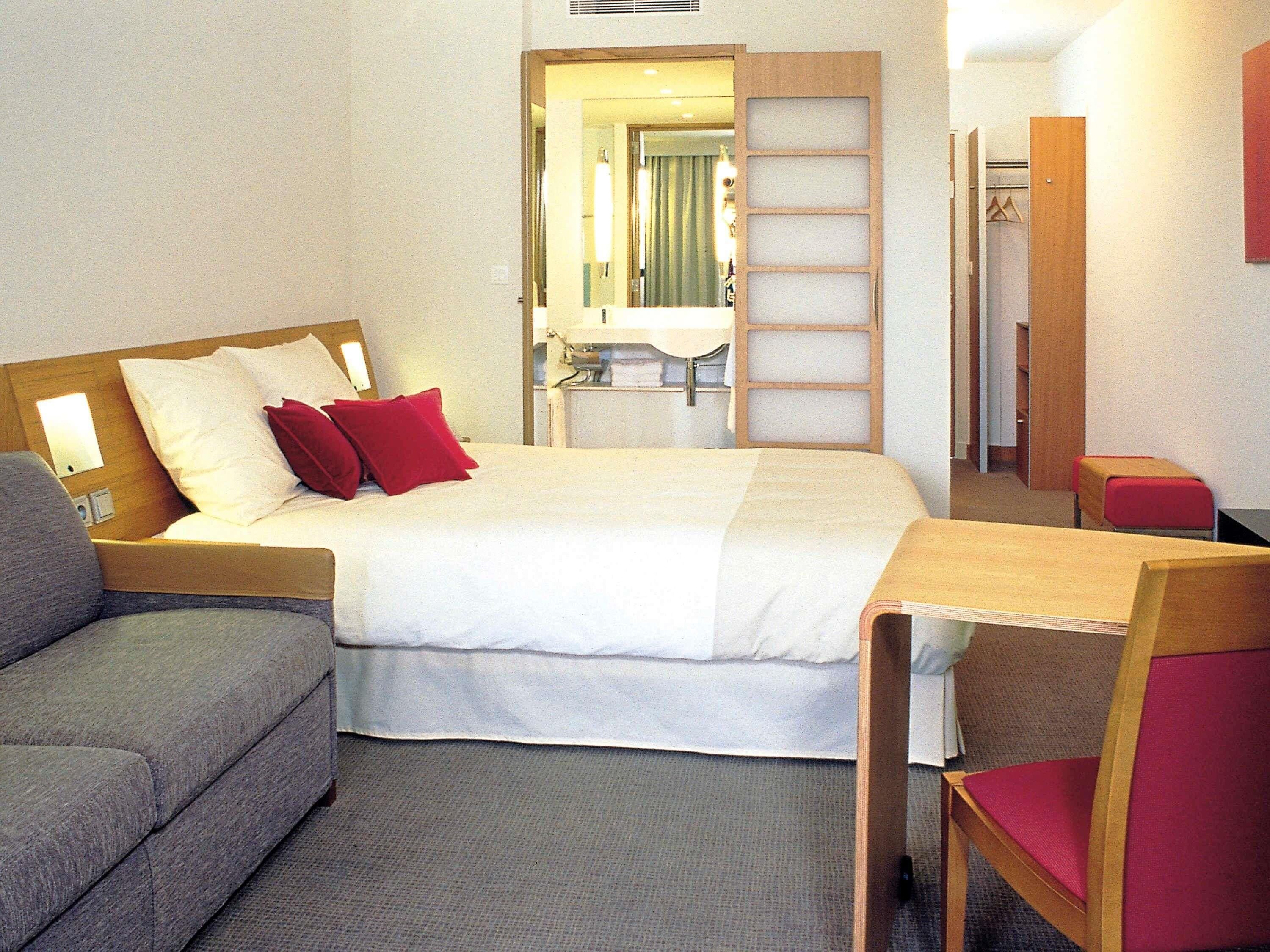 A hotel room with a bed, a desk, a chair, and a sofa.