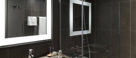 A modern bathroom with a large mirror, a sink, a shower, and dark tiled walls.