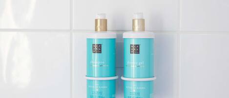 Deux bouteilles du shampooing et du gel douche de la gamme « The Ritual of Karma », posées devant un mur recouvert de carreaux blancs.