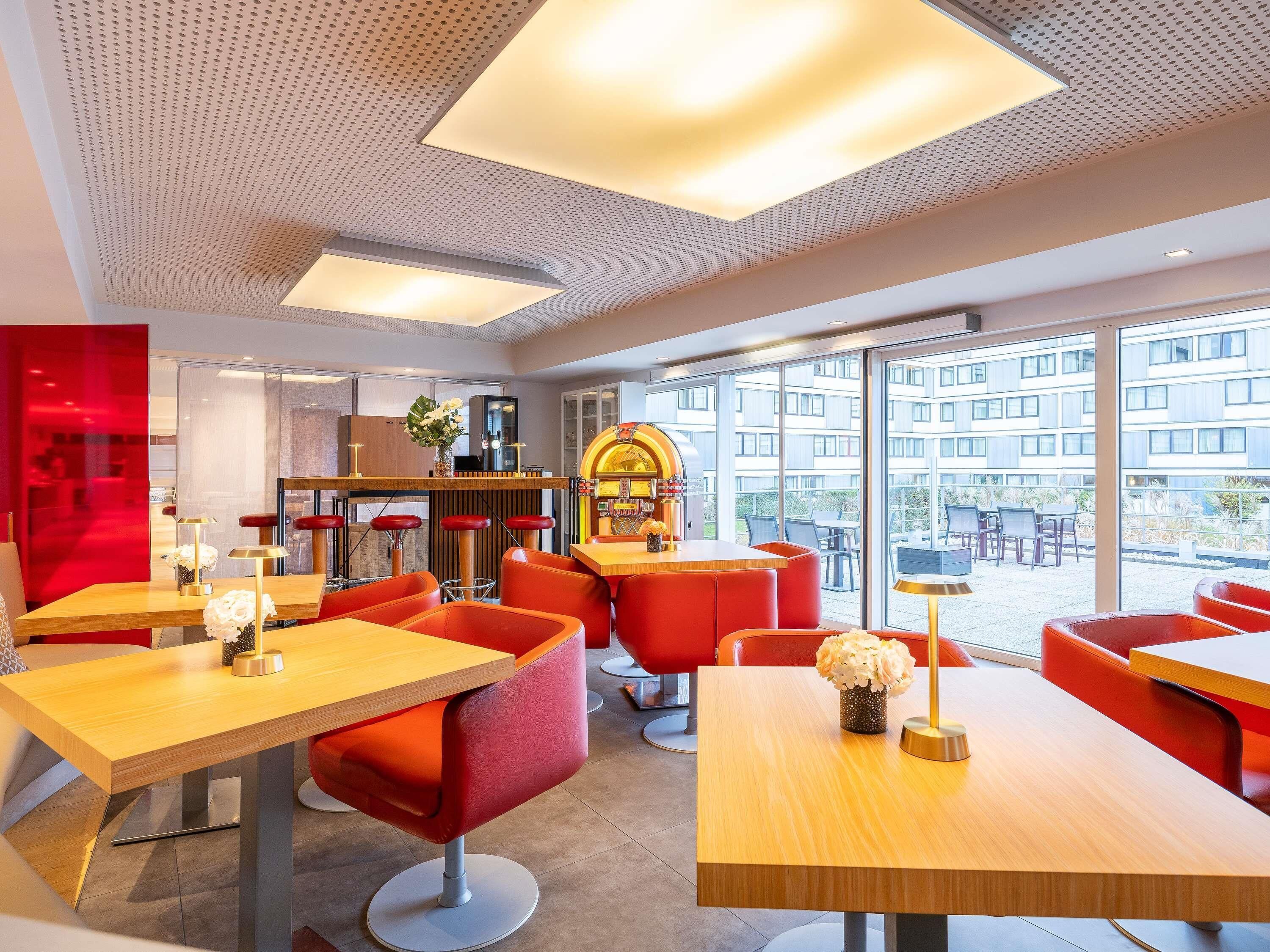 Un restaurante moderno con sillas rojas y mesas de madera, ventanas amplias y una jukebox.