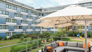 Un hotel moderno con patio en la azotea, mobiliario exterior y un gran paraguas.