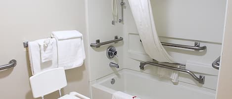 A bathroom with a bathtub, grab bars, a white chair, and a shower curtain.