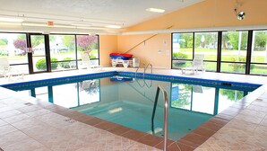 An indoor swimming pool with clear glass walls, a tiled floor, and a pool ladder. - Baymont by Wyndham Springfield (Springfield)