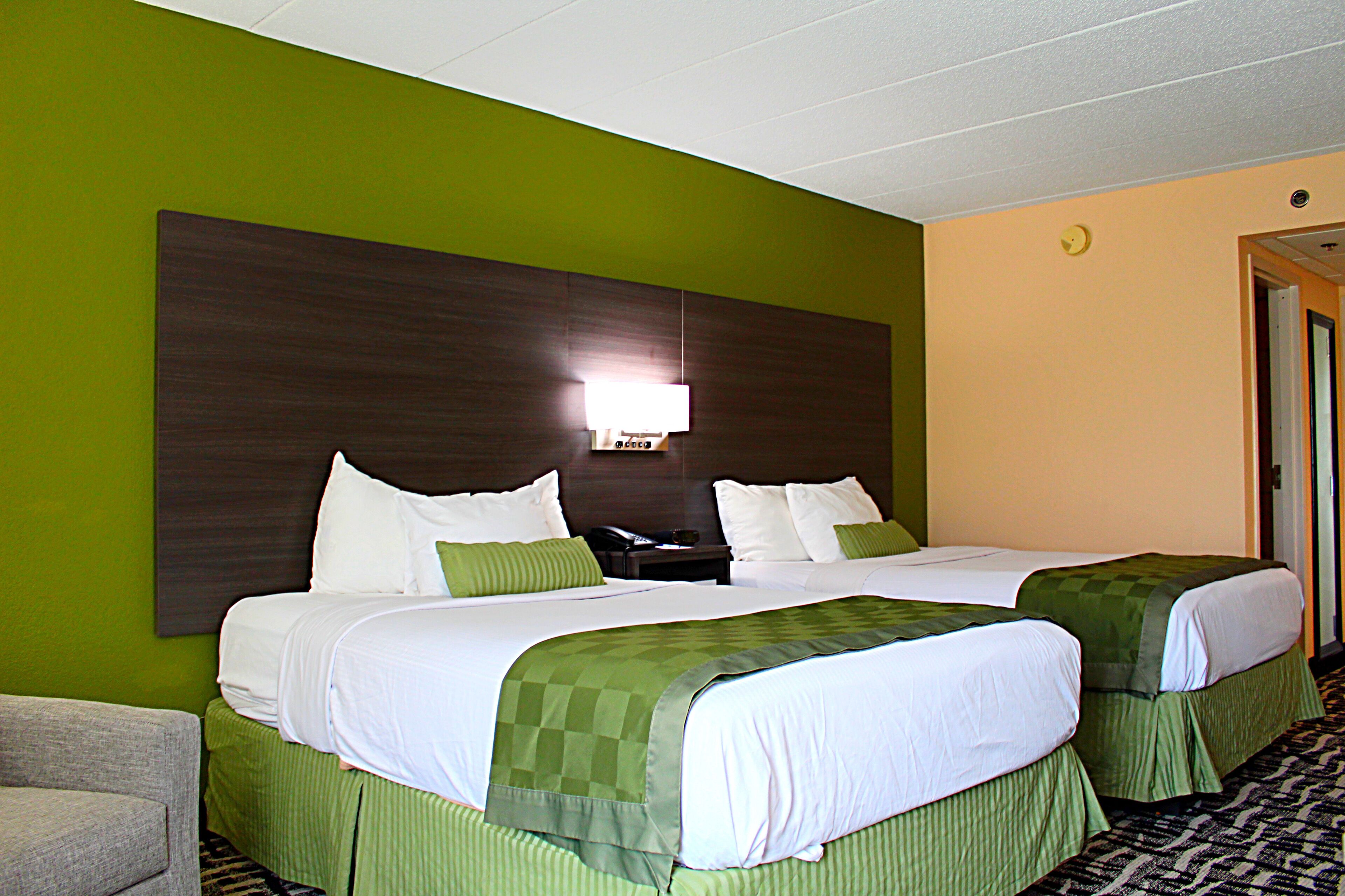 Habitación de hotel con dos camas, ropa de cama verde, un cabecero grande y oscuro, una mesita de noche con teléfono, y un sillón verde.