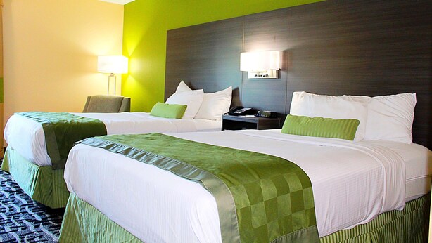 A hotel room with two beds, green bedding, a nightstand with a lamp, and a green accent wall. - Baymont by Wyndham Springfield (Springfield)