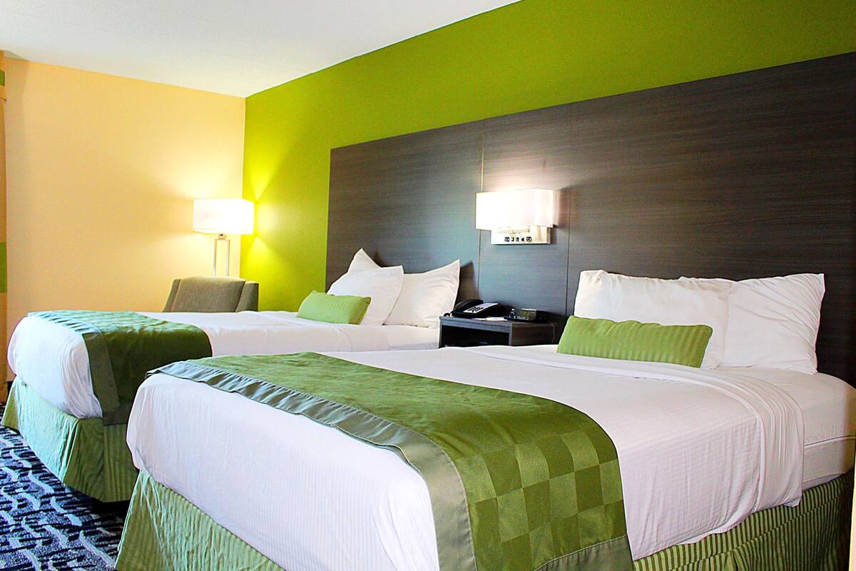 Une chambre d’hôtel avec deux lits, une literie verte, une table de chevet avec une lampe et un mur d’accent vert.