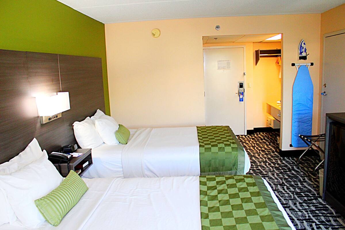 Une chambre d’hôtel avec deux lits, un bureau, une lampe et un tapis à motifs à carreaux.