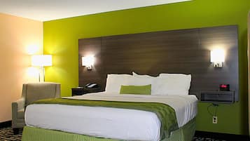 Hotellihuone, jossa on suuri sänky, vihreät seinät, kaksi yöpöytälamppua, tuoli, yöpöytä, jossa on puhelin, ja kello.