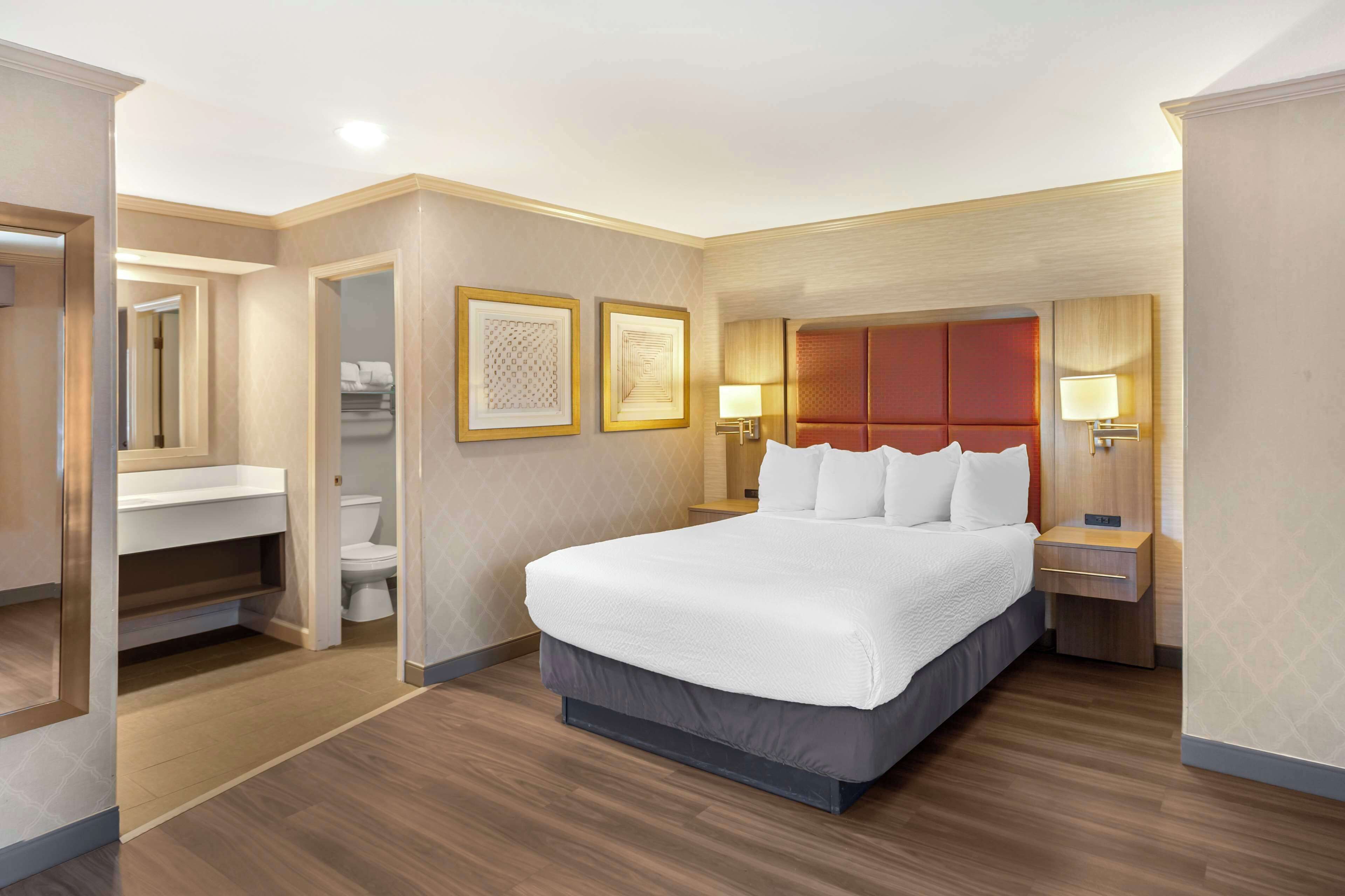 A hotel room with a large bed, a bathroom with a toilet and sink, and a mirror.