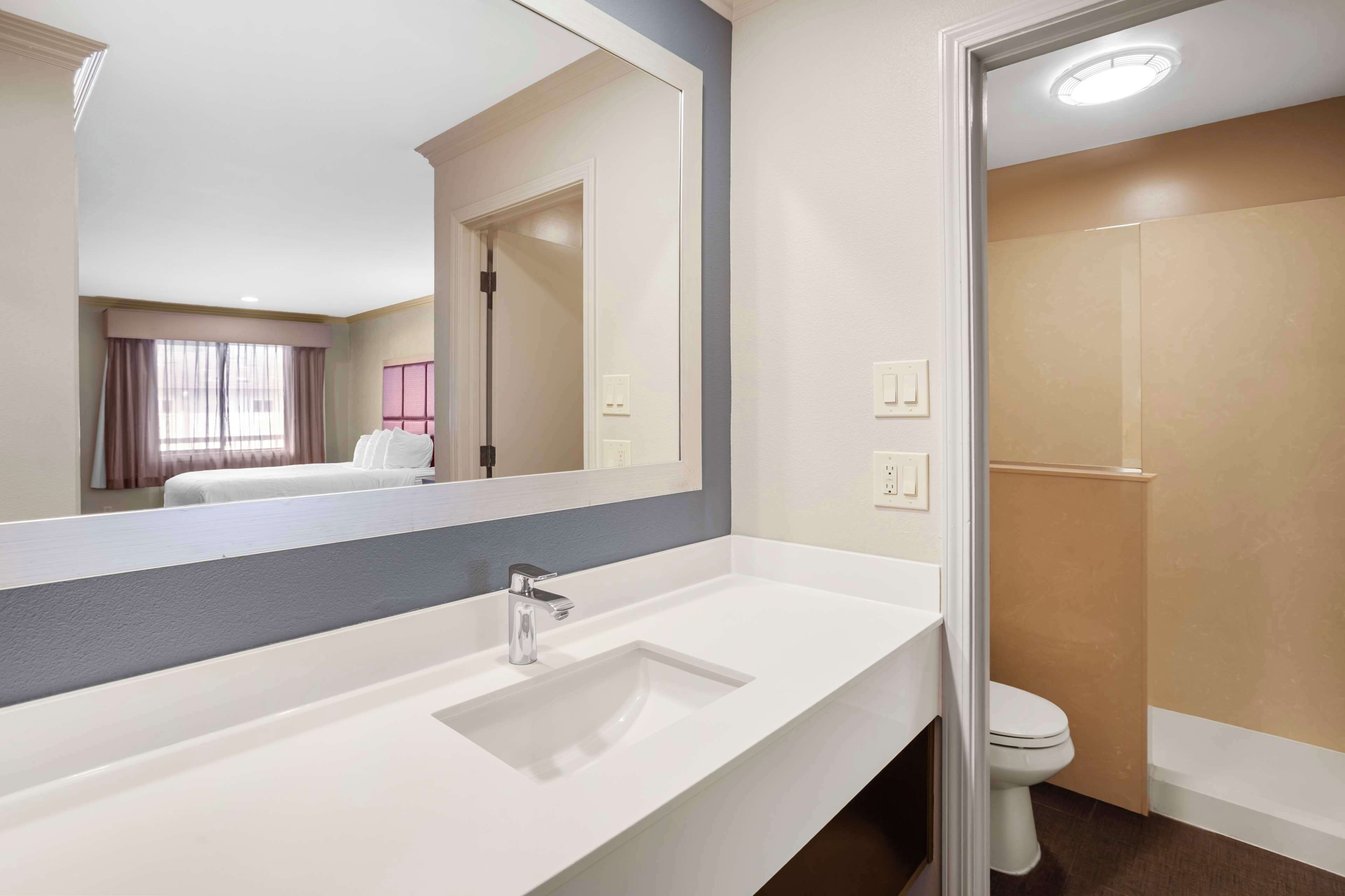 A hotel bathroom with a white sink, a mirror, a toilet, and a shower area.