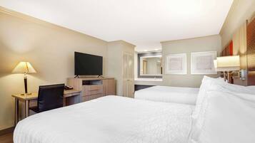 A hotel room with two beds, a desk, a chair, a TV, and a bathroom mirror.