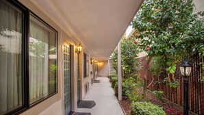 A covered walkway with doors, windows, and a garden area with plants and a fence. - Best Western Inn (Santa Cruz)