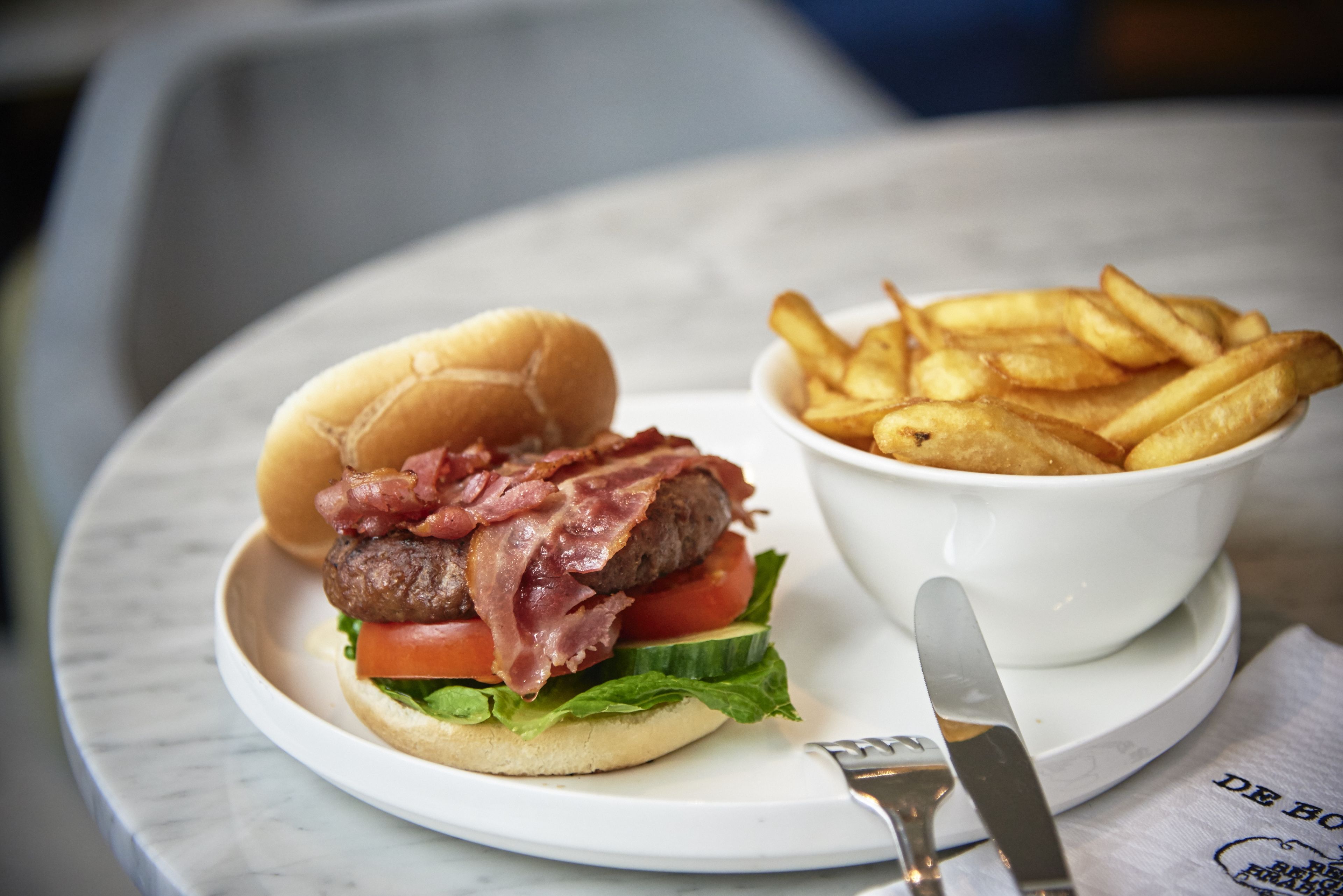 A plate with a burger and fries, a fork, and a knife on a table.