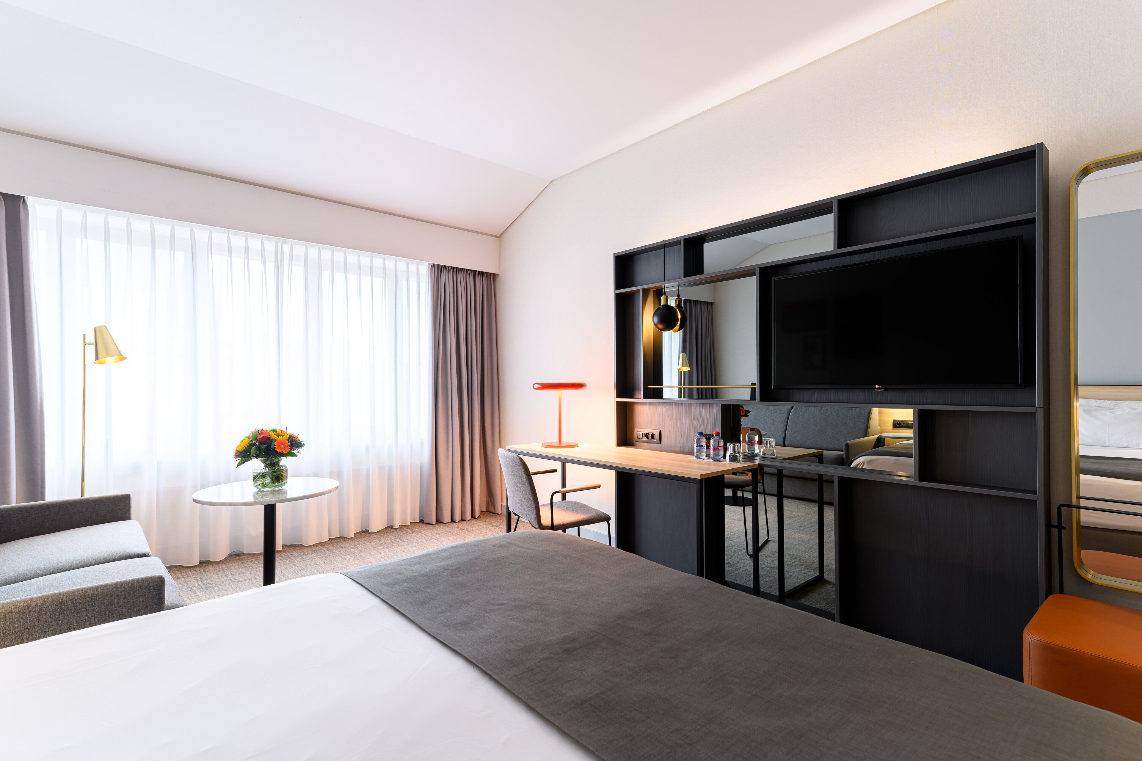 Een moderne hotelkamer met een groot bed, een bureau met stoel, een televisie en een klein tafeltje met een bloevas.