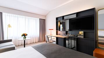 Een moderne hotelkamer met een groot bed, een bureau met stoel, een televisie en een klein tafeltje met een bloevas.