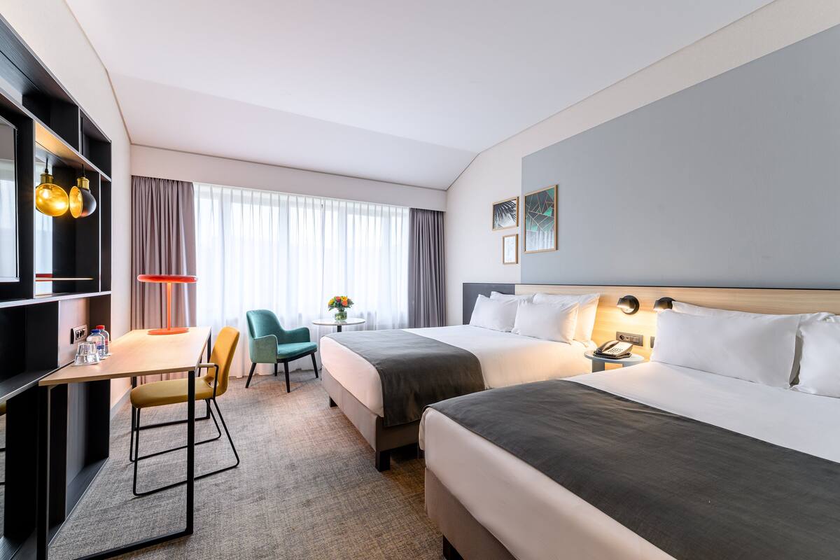 Een hotelkamer met twee bedden, een bureau met stoel, een kleine tafel met bloemenvaas en nachtkastje met lamp.