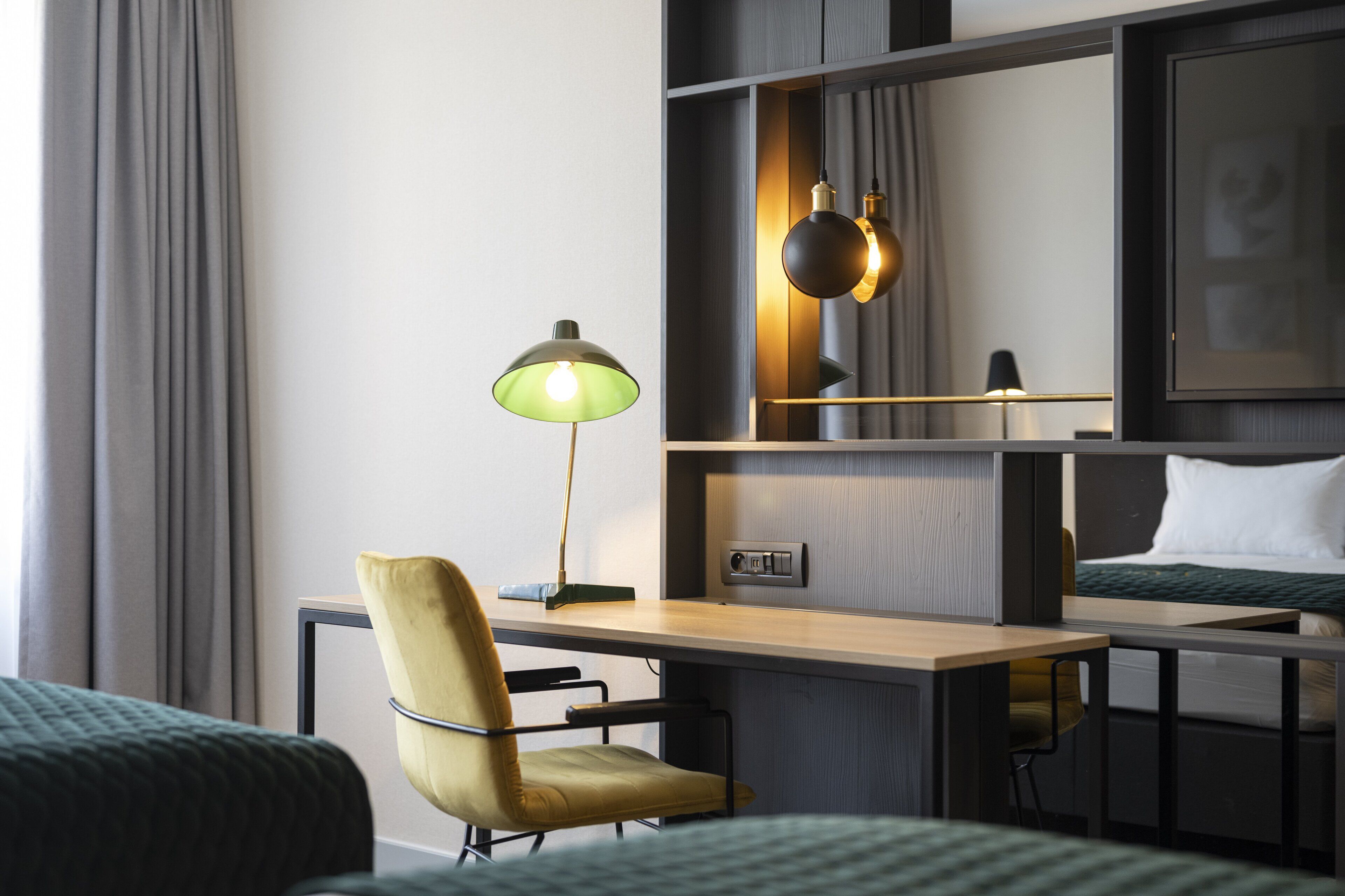 Een hotelkamer met een bureau, twee stoelen, een bed, een lamp en een plank met een foto.