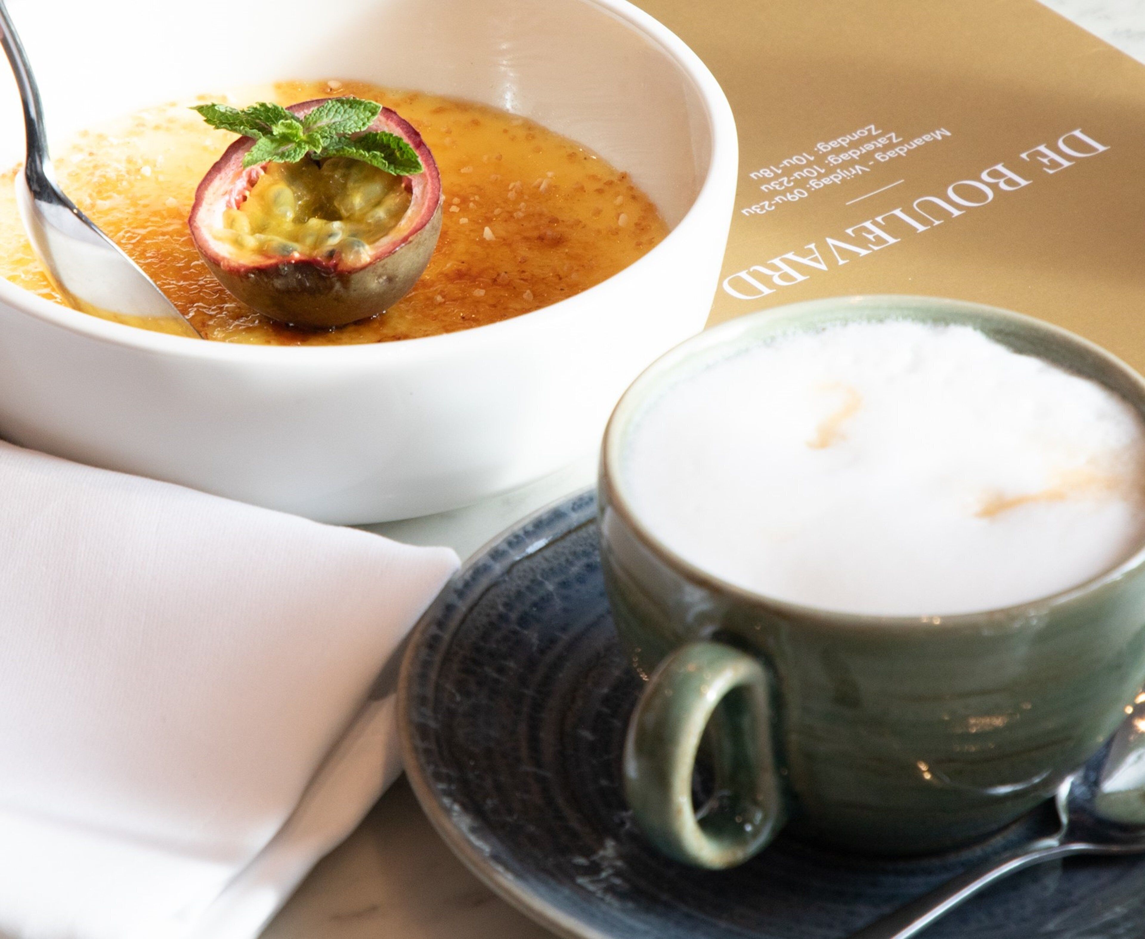 A bowl of soup with a spoon and a cup of coffee on a saucer.