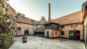 A cobblestone courtyard with brick buildings, a tall chimney, and a wooden barrel. - Holiday Inn Hasselt by IHG (Hasselt)