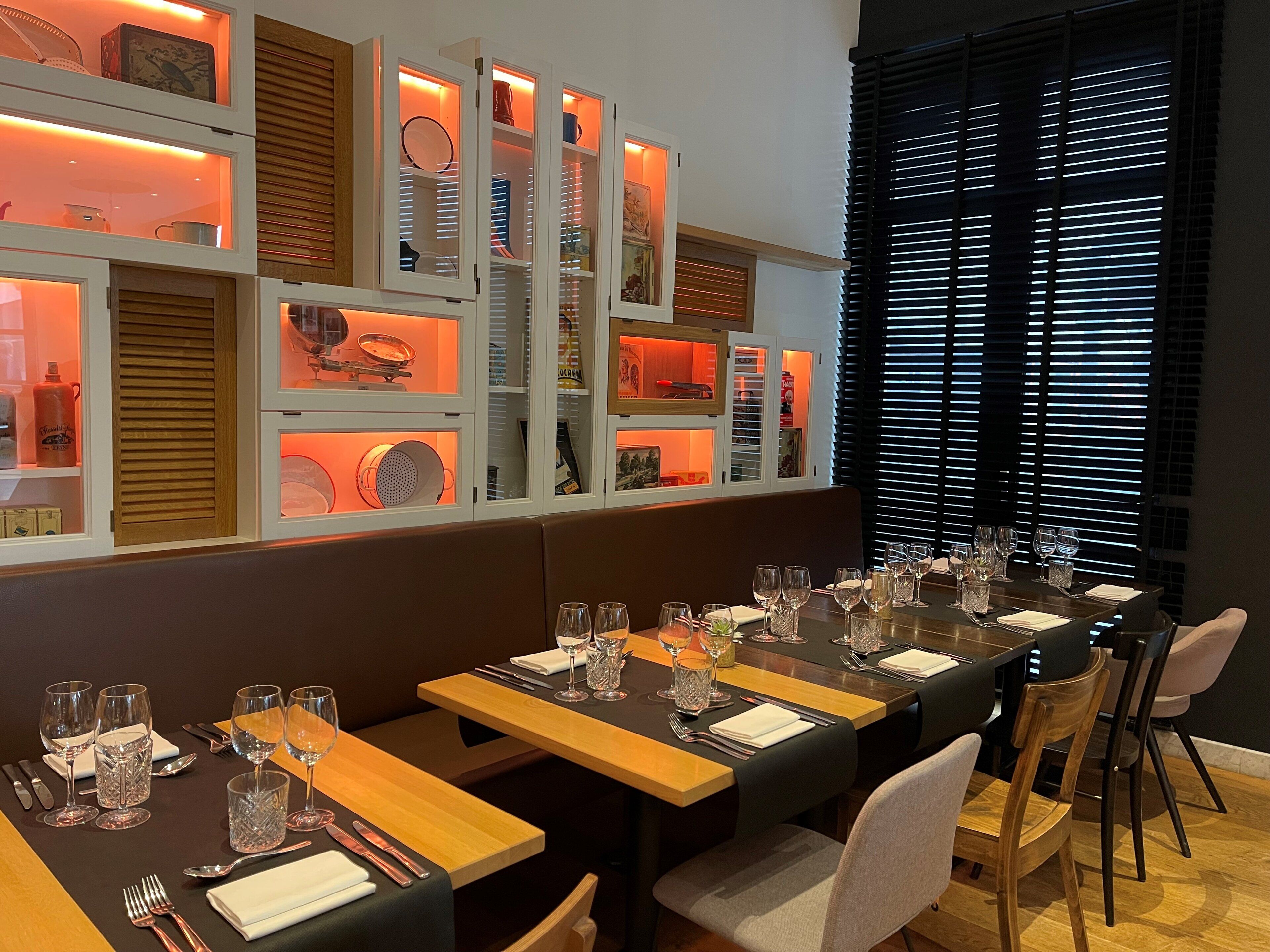 Un restaurante con una larga mesa de comedor dispuesta para una comida, que ofrece diversas opciones de asientos y una pared con estanterías que exhiben varios objetos.
