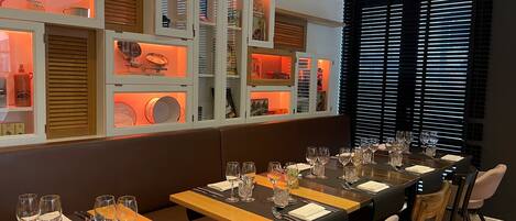Un restaurante con una larga mesa de comedor dispuesta para una comida, que ofrece diversas opciones de asientos y una pared con estanterías que exhiben varios objetos.
