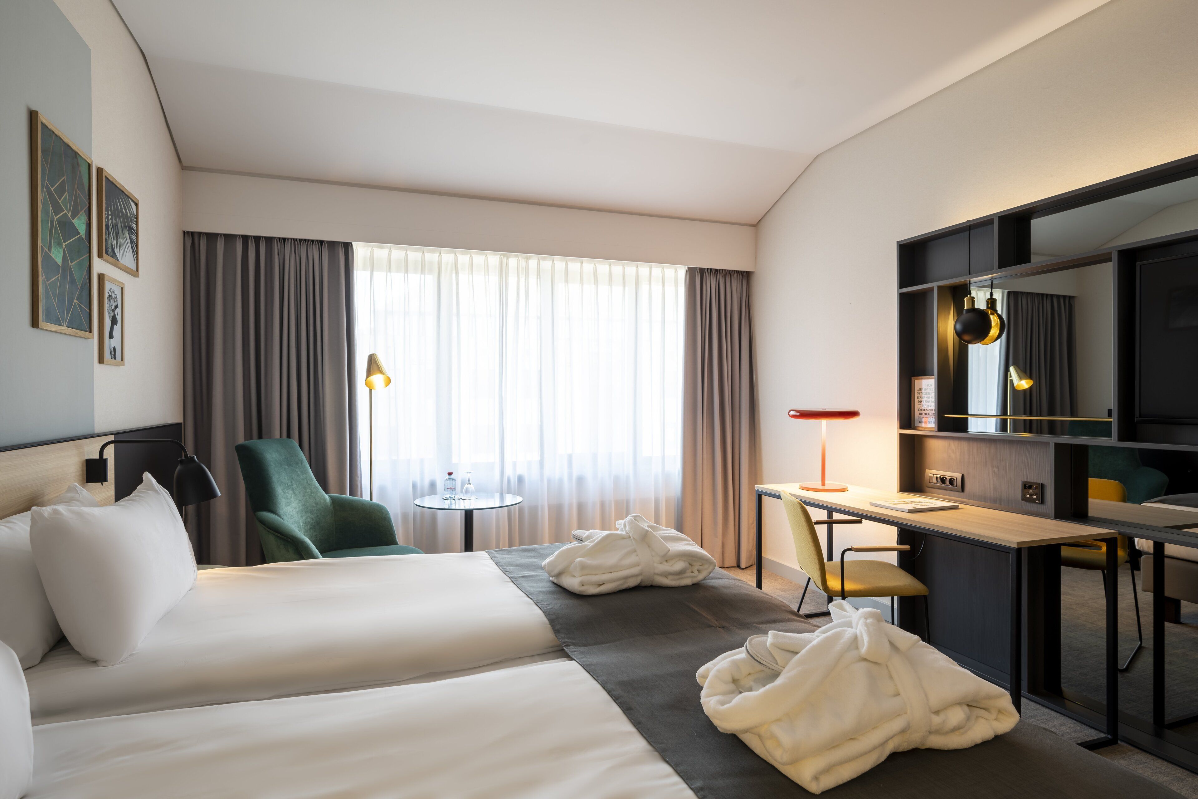 Een hotelkamer met twee bedden, een bureau, een stoel, een televisietoestel en een raam met gordijnen.