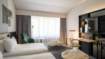 A hotel room with two beds, a desk, a chair, a television, and a window with curtains.
