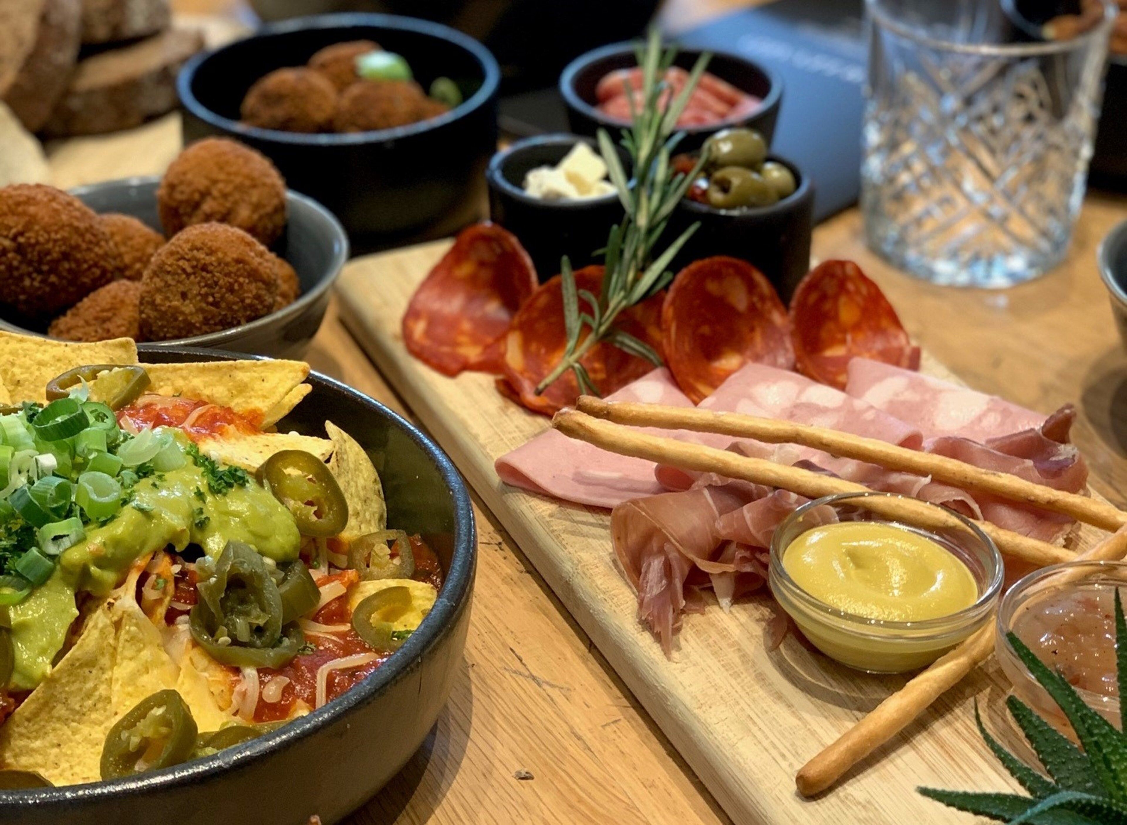 A variety of food items including nachos, sliced meats, and dipping sauces on a wooden table.