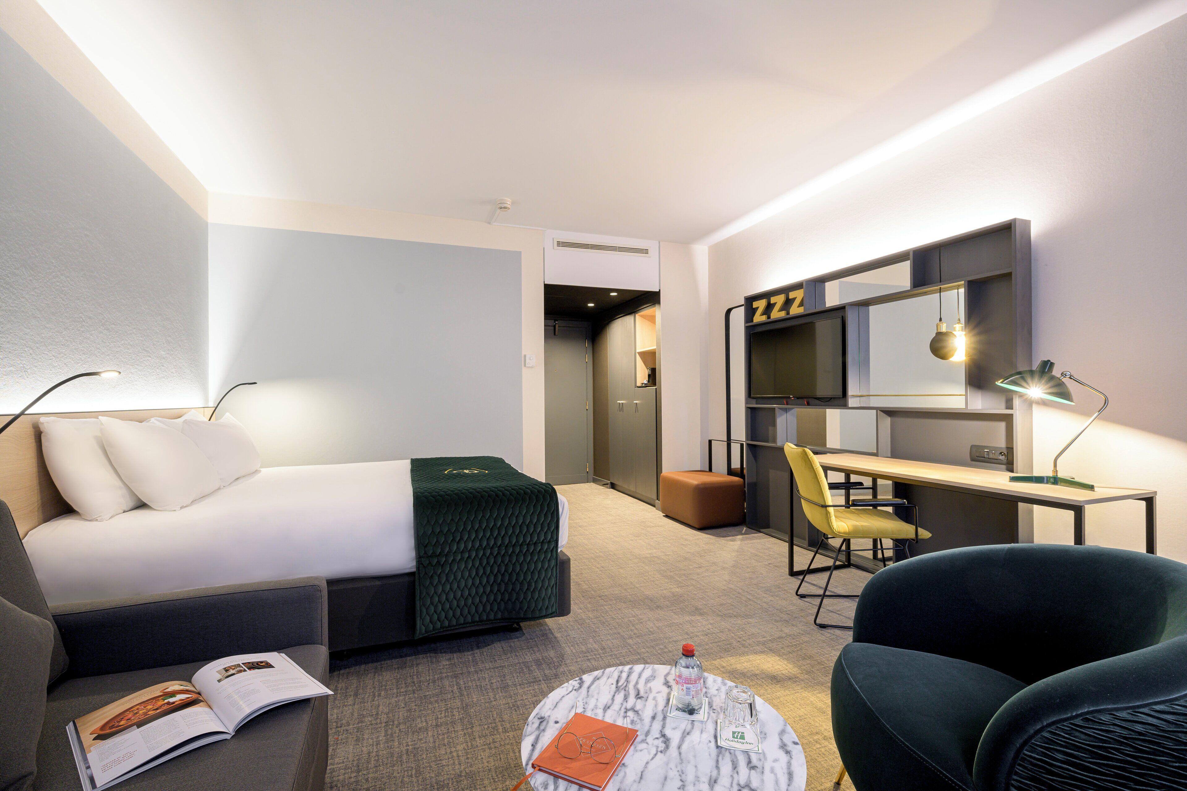 Habitació d'hotel moderna amb un llit, una taula de treball, una cadira, una taula de centre rodona i un espai per llegir.